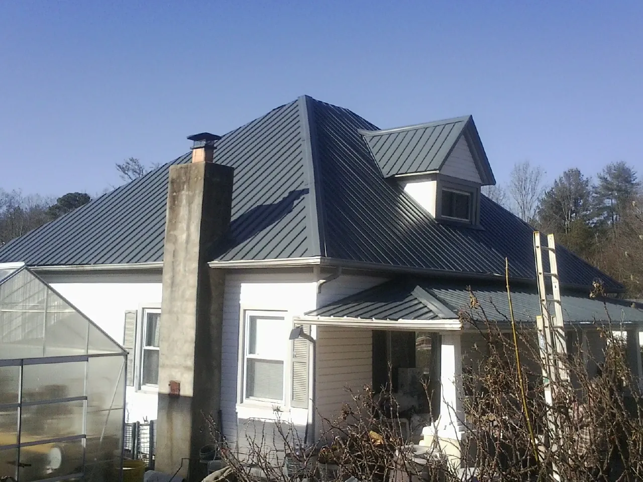 Dark blue standing seam metal roof on a white farmhouse with dormer — Slate & Tile Roof Repair by Roofing Brothers in Haralson