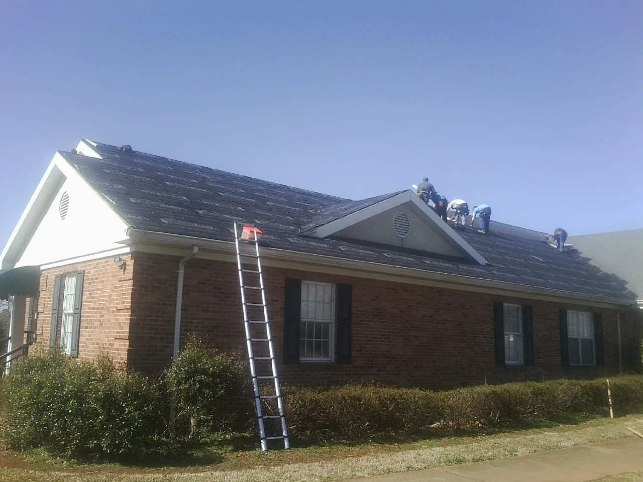 Crew tearing shingles off a brick ranch roof with a ladder set — Emergency Roof Repair work by our crew in Haralson