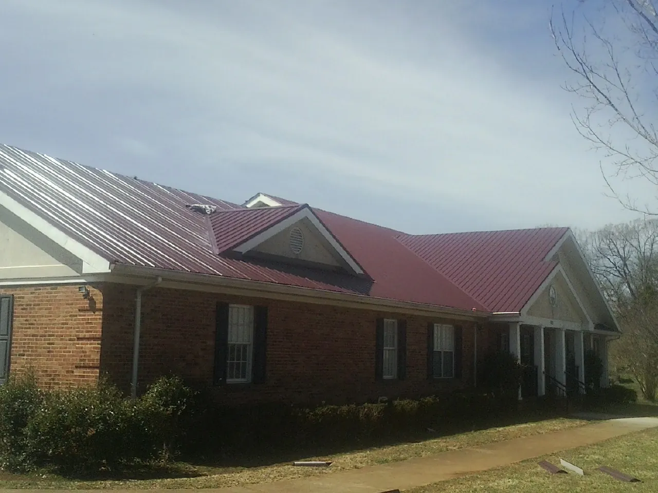 Red metal roof with gabled entries on a long brick building, from a Hail Damage Roof Repair job in Haralson