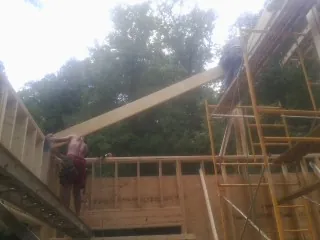 Carpenter raising a rafter beam on a new second story frame in Haralson