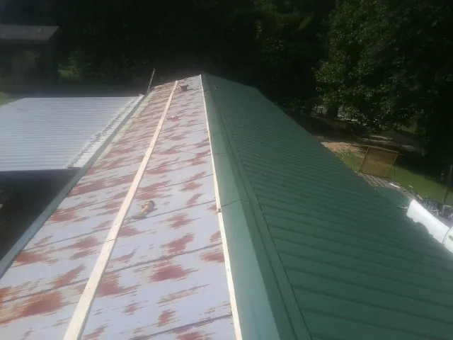Old rusted panels beside newly installed green metal roofing — Wind Damage Roof Repair by Roofing Brothers in Haralson