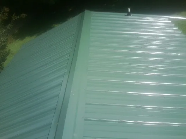 New green metal panels meeting at the ridge of a roof — Flat Roof Repair work by our crew in Haralson
