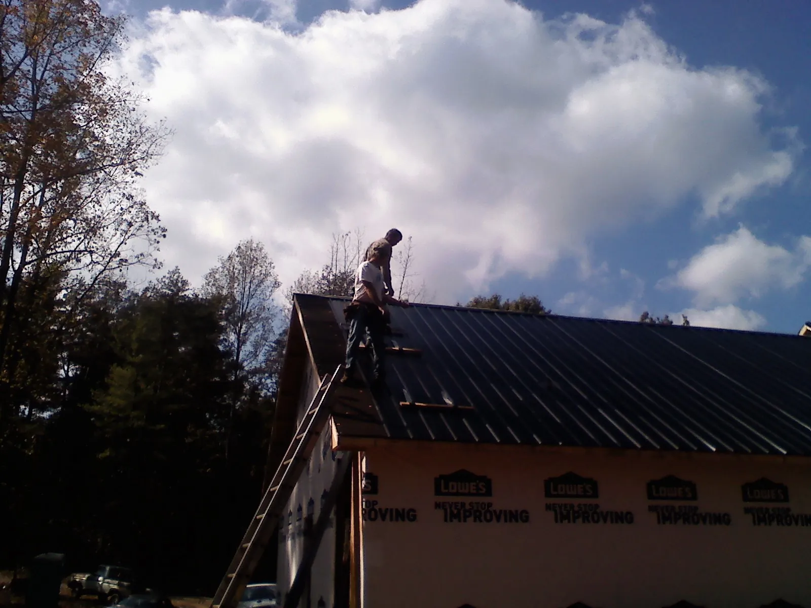 Roofer fastening dark metal panels high against a cloudy sky, from a Roof Inspection job in Haralson