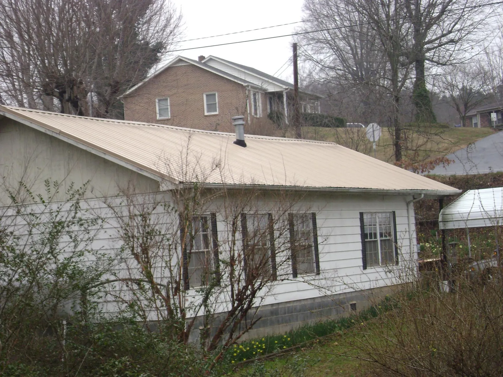Tan metal roof on a white sided house set into a hillside — Commercial Roofing by Roofing Brothers in Haralson