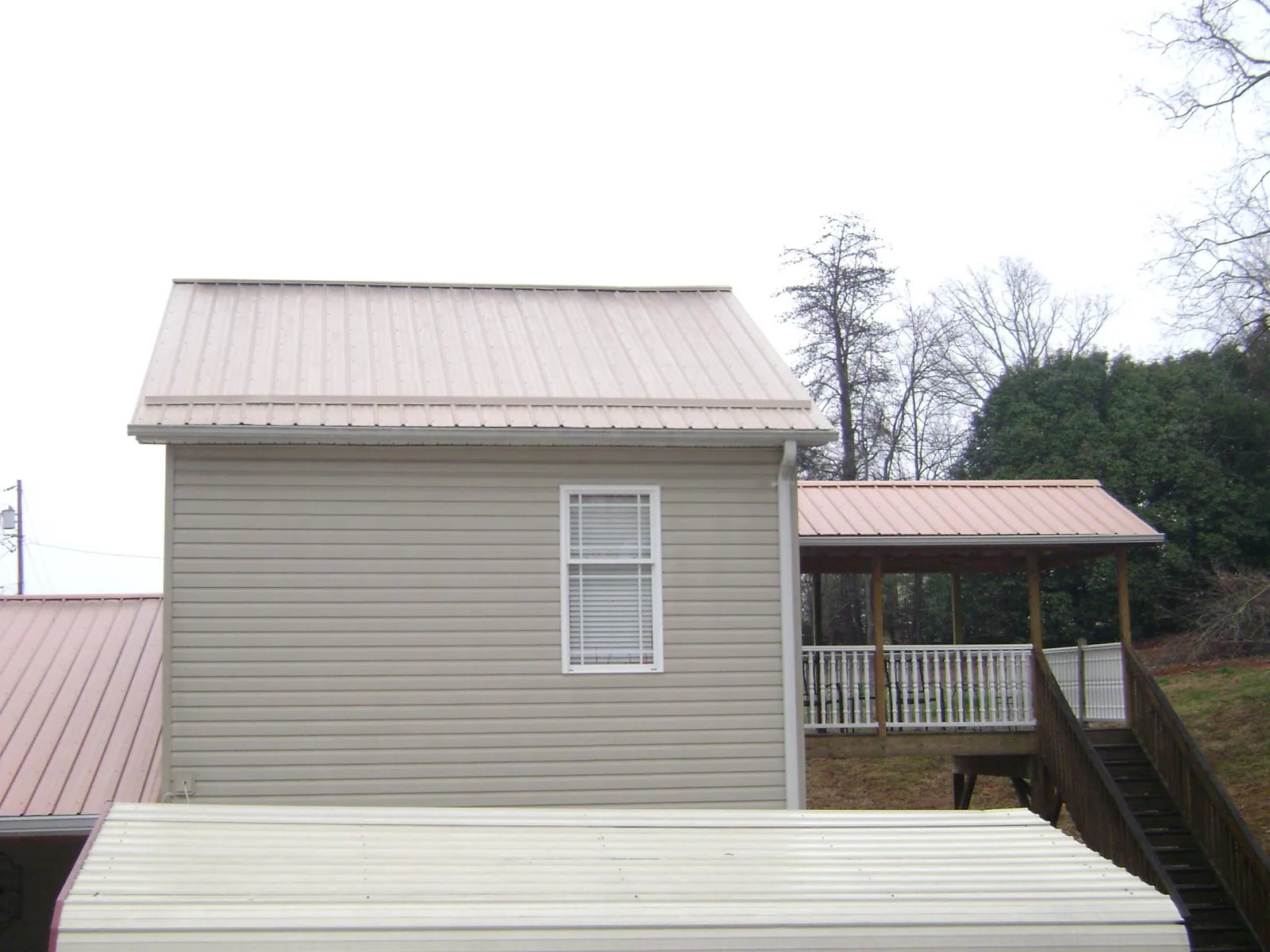 Tan metal roofs on a two story addition and attached porch, from a Roof Replacement job in Haralson